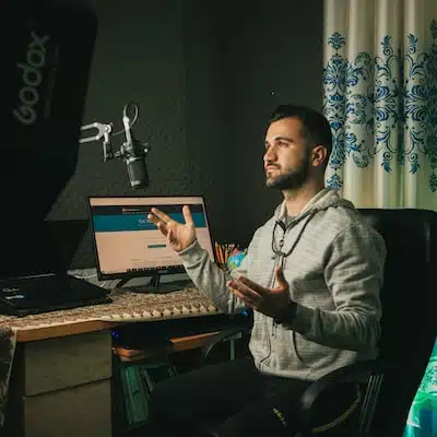 Engaged male YouTuber speaking into a microphone and recording a video at his computer desk, showcasing content creation for the article 'YouTube Revenue Calculator: Calculate Your Earnings Today'